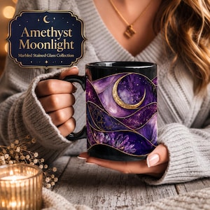 May include: Black ceramic mug featuring a celestial design with a crescent moon and a starry night sky in shades of purple and gold. The mug has the text "Amethyst Moonlight" and "Marbled Stained Glass Collection".
