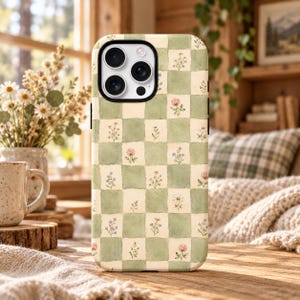 May include: A smartphone case featuring a checkered pattern of alternating sage green and cream squares. Each cream square contains a small, delicate watercolor-style illustration of various wildflowers, including daisies and clover.