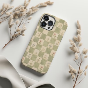 May include: A phone case with a green and cream checkered pattern, adorned with small floral illustrations. The case has a camera cutout and is surrounded by dried floral stems.