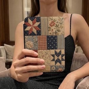 May include: A patchwork tablet case featuring a variety of fabric patterns. The case has a black border and is composed of squares with floral, star, and striped designs in red, blue, and beige tones. The case is held by a person.