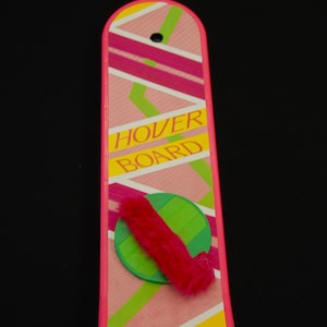 May include: A pink and yellow hoverboard with the words "HOVER BOARD" in yellow. The board has a pink and green design with a red fuzzy detail and a green circle.