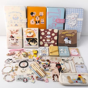 Könnte beinhalten: Eine Sammlung von Schreibwaren und Accessoires zum Thema Hunde, darunter Notizbücher, Stifte, Armbänder, Schlüsselanhänger und Aufkleber. Die Artikel zeigen verschiedene Hundeillustrationen und verspielte Designs in Pastellfarben.