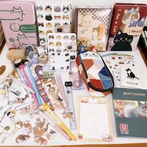 Puede incluir: Una colección de artículos de papelería y accesorios con temática de gatos, que incluyen cuadernos, bolígrafos, pegatinas y un estuche. Los artículos presentan varias ilustraciones y patrones de gatos en una variedad de colores. También hay materiales de arte y un bloc de notas.
