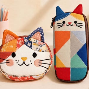 May include: A round, cat-shaped fabric pouch with a patchwork floral pattern and a tall, rectangular cat-shaped pencil case featuring a geometric, multi-colored design. Both items have embroidered facial features, whiskers, and fabric ears.