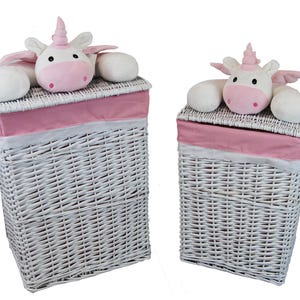 May include: Two white wicker laundry hampers with pink fabric trim and a plush unicorn on top. The unicorns have pink horns, noses, and wings. The hampers are rectangular and have a woven design.