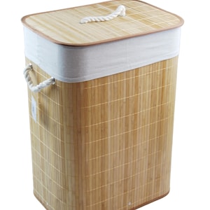 Puede incluir: Una cesta de lavandería rectangular de bambú con tapa a juego. La cesta tiene un forro de tela blanca y asas de cuerda. La tapa tiene un asa de cuerda. La cesta está hecha de bambú marrón claro.