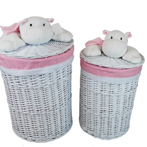 Könnte beinhalten: Zwei weiße Wäschekörbe aus Korbgeflecht mit rosa und weißem Stoffbesatz. Jeder Korb hat ein weißes Nilpferd-Plüschtier auf dem Deckel. Die Körbe sind zylindrisch und haben ein gewebtes Design.