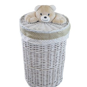 Könnte beinhalten: Ein weißer Wäschekorb aus Korbgeflecht mit einem beigen Teddybären auf dem Deckel. Der Korb hat eine zylindrische Form und ist mit einem beige-weiß gepunkteten Stoffbesatz versehen. Höhe ca. 76 cm.