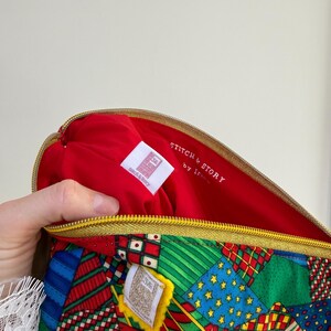 Peut inclure: Une pochette zipp&eacute;e &agrave; motifs avec un int&eacute;rieur rouge. L'ext&eacute;rieur pr&eacute;sente un motif patchwork avec des accents rouges, verts, bleus et jaunes. L'int&eacute;rieur porte l'inscription "STITCH & STORY by Iris" sur une &eacute;tiquette blanche.