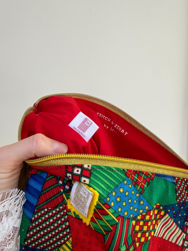 Peut inclure: Une pochette zipp&eacute;e &agrave; motifs avec un int&eacute;rieur rouge. L'ext&eacute;rieur pr&eacute;sente un motif patchwork avec des accents rouges, verts, bleus et jaunes. L'int&eacute;rieur porte l'inscription "STITCH & STORY by Iris" sur une &eacute;tiquette blanche.