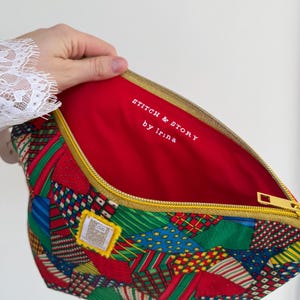 Peut inclure: Une pochette zipp&eacute;e en patchwork avec un int&eacute;rieur rouge. L'ext&eacute;rieur pr&eacute;sente un m&eacute;lange de tissus &agrave; motifs rouges, verts, bleus et blancs. La fermeture &eacute;clair est dor&eacute;e et l'int&eacute;rieur porte l'inscription "STITCH & STORY by Irina".
