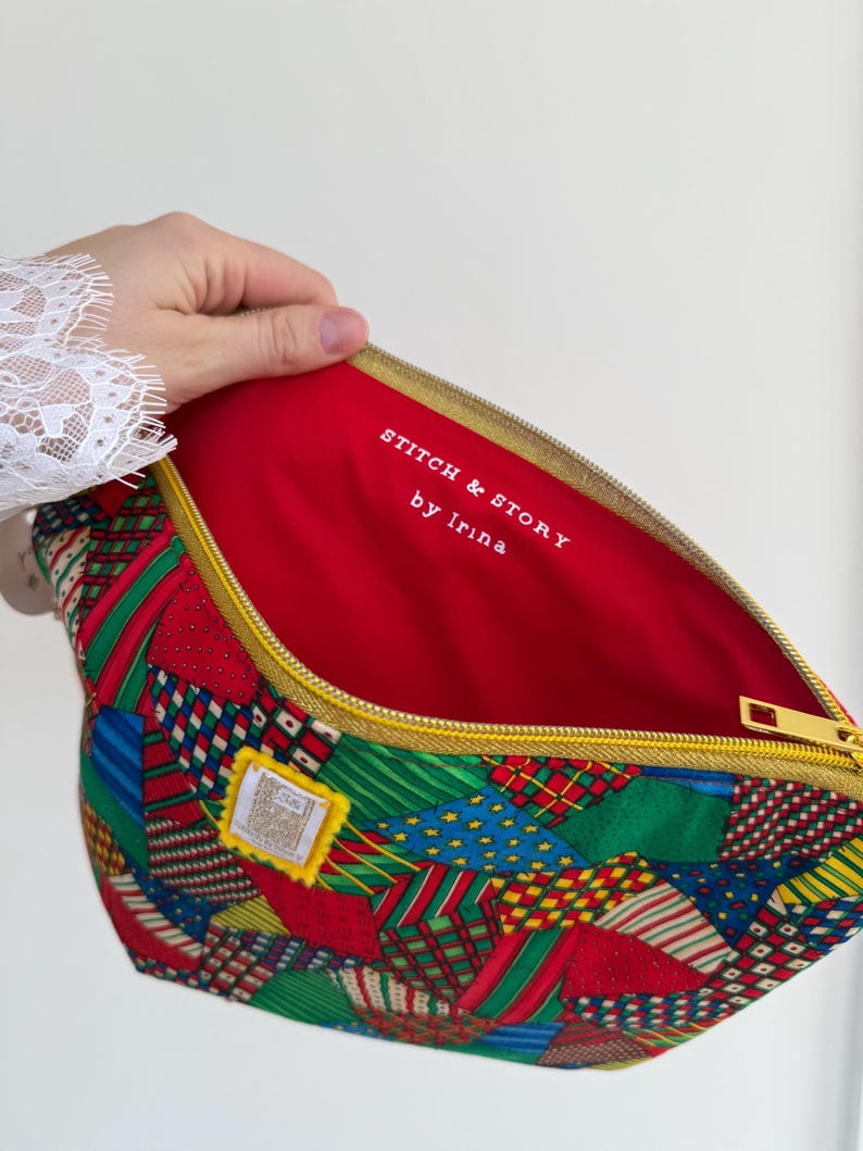 Peut inclure: Une pochette zipp&eacute;e en patchwork avec un int&eacute;rieur rouge. L'ext&eacute;rieur pr&eacute;sente un m&eacute;lange de tissus &agrave; motifs rouges, verts, bleus et blancs. La fermeture &eacute;clair est dor&eacute;e et l'int&eacute;rieur porte l'inscription "STITCH & STORY by Irina".