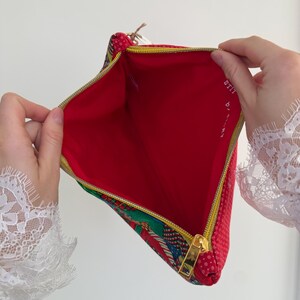 Peut inclure: Pochette zipp&eacute;e rouge et &agrave; motifs avec une fermeture &eacute;clair dor&eacute;e. L'int&eacute;rieur est rouge, et l'ext&eacute;rieur pr&eacute;sente un motif &agrave; pois rouges et un motif color&eacute;. Le texte "STITCH by ART" est visible &agrave; l'int&eacute;rieur de la pochette.
