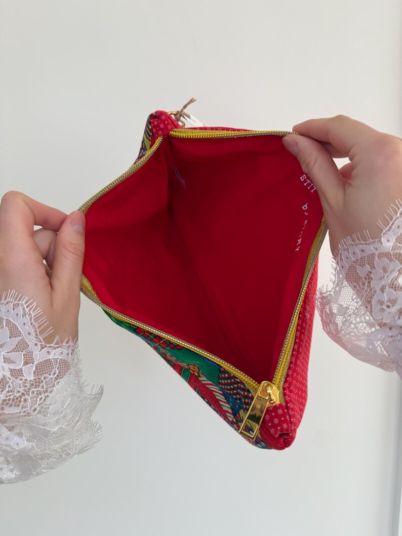 Peut inclure: Pochette zipp&eacute;e rouge et &agrave; motifs avec une fermeture &eacute;clair dor&eacute;e. L'int&eacute;rieur est rouge, et l'ext&eacute;rieur pr&eacute;sente un motif &agrave; pois rouges et un motif color&eacute;. Le texte "STITCH by ART" est visible &agrave; l'int&eacute;rieur de la pochette.