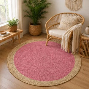 Könnte beinhalten: Ein runder Teppich mit rosa Mitte und einem Rand aus Naturfaser. Der Teppich liegt auf einem Holzboden, mit einem Korbstuhl und einem Beistelltisch. Der Durchmesser des Teppichs beträgt ca. 152 cm.