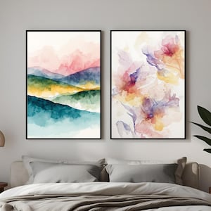 Può includere: Due stampe artistiche ad acquerello incorniciate. Una raffigura un paesaggio montano nei toni del rosa, blu, verde e giallo. L'altra presenta arte floreale astratta in rosa, giallo e viola. Le stampe sono appese sopra un letto con una coperta grigia.