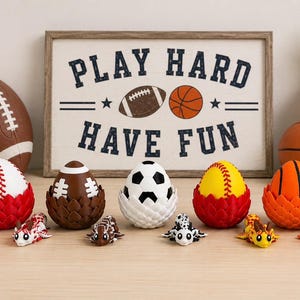 May include: Five sports-themed eggs in textured holders, including baseball, football, soccer, softball, and basketball designs. Each egg is paired with a small, matching articulated dragon figurine. A framed sign reads PLAY HARD HAVE FUN.