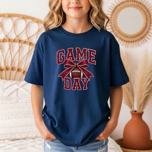 Youth True Navy Comfort Colors Game Day football shirt with a maroon bow graphic.