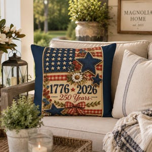 May include: A square throw pillow featuring a patriotic design with a red and white gingham border, blue stars, and floral accents. The center displays the text 1776 2026 250 Years with a small red star between the dates and a red gingham bow below.
