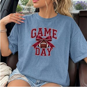 Woman wearing a Blue Jean Comfort Colors Game Day t-shirt featuring a maroon football bow.