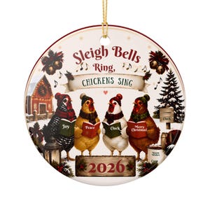 Peut inclure: Une décoration de Noël ronde en céramique représentant quatre poules portant des bonnets et des écharpes d'hiver, tenant des livres de chants marqués Joy, Peace, Cluck et Merry Christmas. Le texte indique Sleigh Bells Ring, CHICKENS SING et 2026.