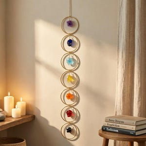May include: A vertical wall hanging featuring seven gold-toned metal rings arranged in a column. Each ring contains a single raw crystal suspended in the center, displaying a spectrum of colors including purple, blue, light blue, yellow, orange, red, and black.