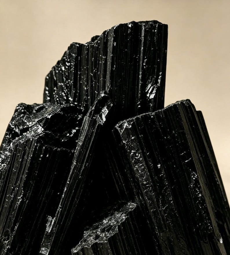 Puede incluir: Un grupo de cristales de turmalina negra en bruto con estr&iacute;as verticales profundas y una superficie brillante y reflectante. La formaci&oacute;n mineral muestra bordes afilados y dentados, junto con un color oscuro y opaco muy caracter&iacute;stico.