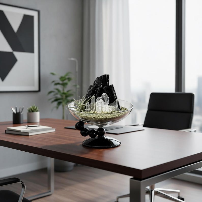 Puede incluir: Un centro de mesa de cuenco de cristal transparente con cristales de turmalina negra y cuarzo transparente sobre una base de peque&ntilde;as piedras verdes. El cuenco se apoya en una base negra con un dise&ntilde;o de esferas apiladas como decoraci&oacute;n.
