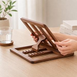 Pu&ograve; includere: Un leggio in legno marrone scuro con un supporto angolato regolabile. Il leggio ha una base rettangolare e fessure per tenere aperto un libro. Il leggio &egrave; in fase di regolazione da una persona.