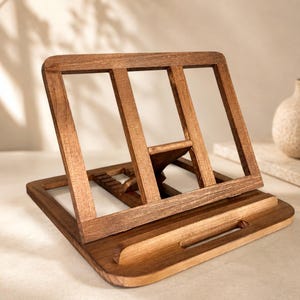 Pu&ograve; includere: Un leggio in legno con finitura marrone caldo. Il leggio presenta un design inclinato con un bordo per tenere aperto un libro. Il retro ha dei supporti verticali. La base ha un ritaglio curvo per una penna.