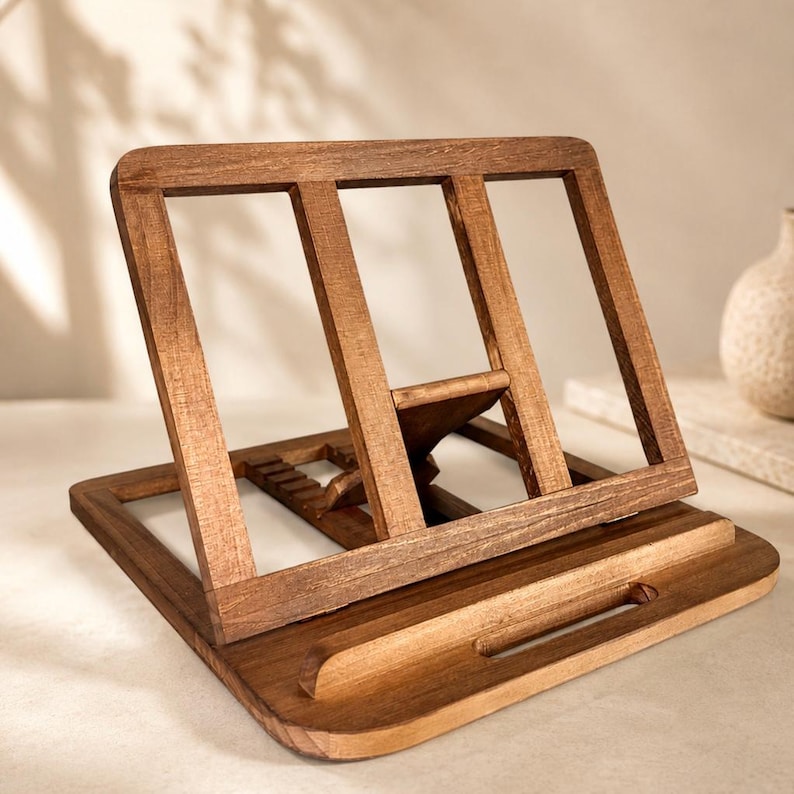 Pu&ograve; includere: Un leggio in legno con finitura marrone caldo. Il leggio presenta un design inclinato con un bordo per tenere aperto un libro. Il retro ha dei supporti verticali. La base ha un ritaglio curvo per una penna.