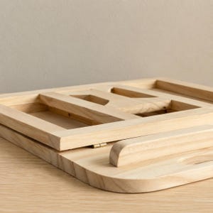 Pu&ograve; includere: Una scrivania portatile in legno chiaro con una cornice rettangolare e un bordo curvo. La scrivania ha un design a cerniera per piegare e riporre. La cornice ha sezioni ritagliate.