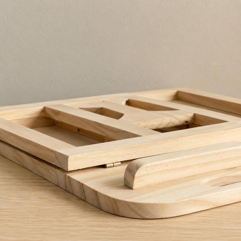 Pu&ograve; includere: Una scrivania portatile in legno chiaro con una cornice rettangolare e un bordo curvo. La scrivania ha un design a cerniera per piegare e riporre. La cornice ha sezioni ritagliate.