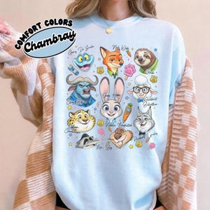 Comfort Colors Chambray blue Zootopia sweatshirt with a high-quality character collage. This light blue pastel top features Judy Hopps and Nick Wilde surrounded by fun movie icons like carrots and stars. The retro aesthetic makes it a stylish choice for cooler days at Animal Kingdom or Hollywood Studios. Shown layered with a tan checkered cardigan, this trendy Disney outfit is perfect for fans who love a cozy, oversized fit. Durable and soft, it’s a unique gift for any Zootopia enthusiast.