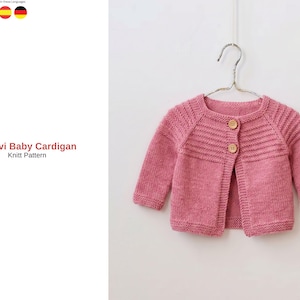 May include: A pink baby cardigan with a round neckline and long sleeves, hanging on a metal hanger. The knitted sweater has wooden buttons and horizontal ribbed detailing across the chest. The text "Demavi Baby Cardigan Knit Pattern" is visible.
