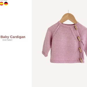 May include: A light pink baby cardigan with wooden buttons, displayed on a wooden hanger. The knitted sweater has a textured design on the shoulders and the text "Mujde Baby Cardigan Knitt Pattern" is visible.
