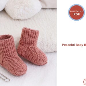 Könnte beinhalten: Zwei handgestrickte Baby-Booties in einem staubigen Rosaton. Die Booties sind aus weichem, strukturiertem Garn gefertigt und haben einen gerippten Bund. Der Text "Peaceful Baby Booties" ist im Bild zu sehen. Eine Büroklammer liegt daneben.