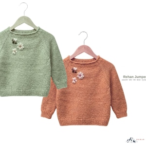 Puede incluir: Dos suéteres infantiles en perchas. Uno es verde salvia, el otro es de color óxido. Ambos tienen adornos florales cerca del cuello. El texto "Rehan Jumper Sweater" y la información de tallas son visibles.