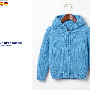 Könnte beinhalten: Hellblauer, gestrickter Kinderhoodie mit Reißverschluss, hängt an einem Holzbügel. Der Hoodie hat eine Kapuze und besteht aus einem grob gestrickten Material. Der Text "Kudret Children Hoodie Knitt Pattern" ist sichtbar.