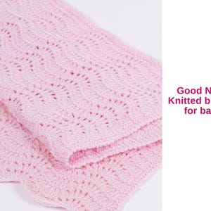 May include: A soft, pink knitted baby blanket with a delicate wave pattern. The blanket is folded, showcasing the intricate knit design. Text on the side reads "Good Night Knitted blanket for baby."