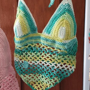 Pu&ograve; includere: Un top all'americana lavorato all'uncinetto a mano con corpetto triangolare in un gradiente di filato bianco, verde lime e verde acqua. La parte inferiore presenta un motivo a rete aperta, rifinito con un orlo a punta e piccoli fiori.