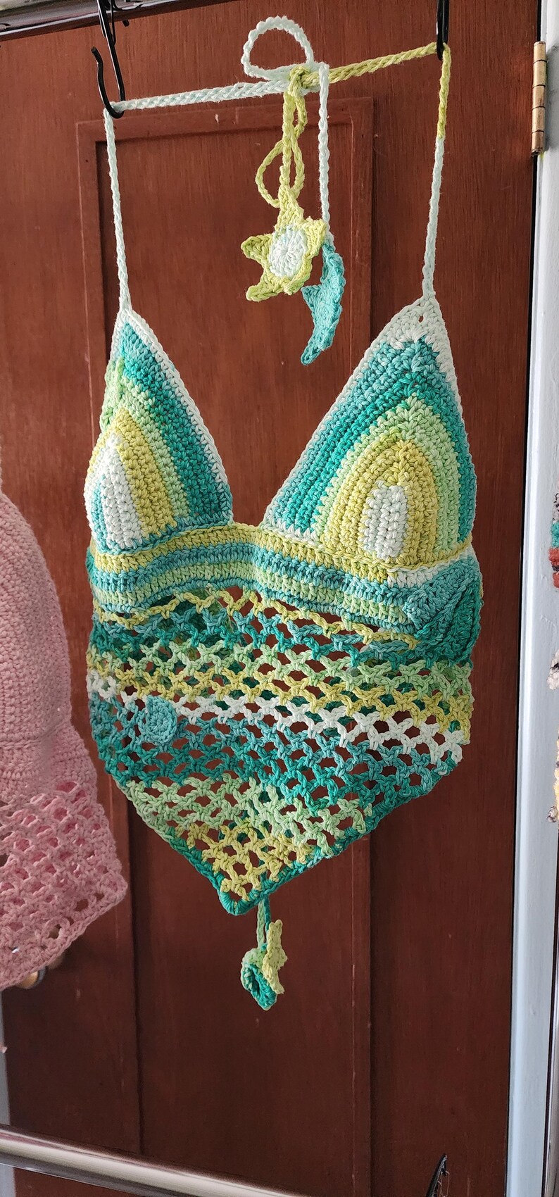 Pu&ograve; includere: Un top all'americana lavorato all'uncinetto a mano con corpetto triangolare in un gradiente di filato bianco, verde lime e verde acqua. La parte inferiore presenta un motivo a rete aperta, rifinito con un orlo a punta e piccoli fiori.