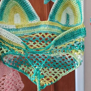 Pu&ograve; includere: Un top all'americana all'uncinetto con un design triangolare e strisce orizzontali nei toni del verde, giallo e bianco. La parte inferiore presenta un motivo a rete aperta e le spalline sono decorate con piccole stelle all'uncinetto.