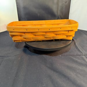May include: A rectangular woven basket made of light brown wood strips. The basket features a reinforced top rim secured with small metal rivets along the sides. The base is flat and the walls are constructed with an overlapping horizontal weave pattern.