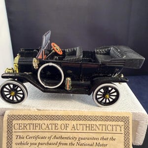 Puede incluir: Modelo de coche antiguo negro con ruedas con borde blanco y volante rojo. El modelo tiene detalles dorados y un certificado de autenticidad. El coche es un objeto de colección.