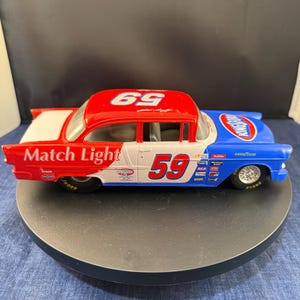 以下が含まれることがあります： 赤、白、青のヴィンテージおもちゃのレーシングカー。車体には赤で59番、側面に「Match Light」の文字が入っています。屋根は赤で69番。クラシックなモデルです。