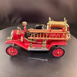 Puede incluir: Un camión de bomberos rojo en miniatura con detalles dorados. El juguete incluye una escalera, un carrete de manguera y ruedas detalladas. El vehículo es un modelo de estilo vintage.