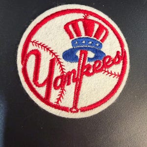 May include: Embroidered patch featuring the New York Yankees logo. The design includes a red baseball bat, the word "Yankees" in red script, and a red, white, and blue Uncle Sam hat. The patch is circular with a white background and red border.
