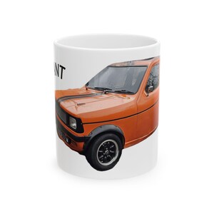 Puede incluir: Taza de cerámica blanca con un coche naranja vintage con rayas negras y ruedas negras. El coche tiene una parrilla delantera negra y ensanchadores de guardabarros negros. La palabra "ANT" es parcialmente visible.