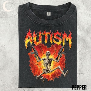 Puede incluir: Camiseta gris oscuro con la palabra "AUTISMO" en letras de fuego, que representa un esqueleto sosteniendo dos ametralladoras sobre un fondo rojo y naranja. La palabra "PEPPER" está en la parte inferior.